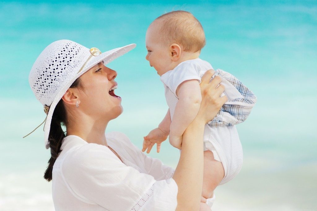 海辺で女性が赤ちゃんを抱きあげ微笑みあう写真